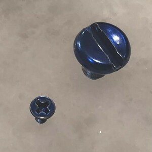 May include: Two blue screws of different sizes. The larger screw has a slotted head, while the smaller screw has a Phillips head. Both screws have a shiny, metallic finish and are set against a light-colored background.