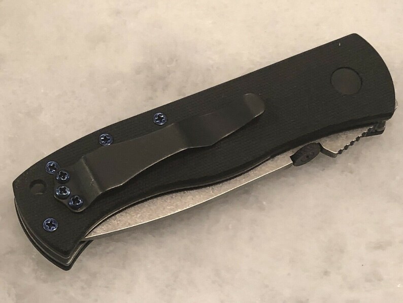 May include: Black pocket knife with a black clip and blue screws. The knife has a partially serrated blade.