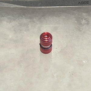 Peut inclure: Un bouchon de bouteille en métal rouge avec une bande argentée.