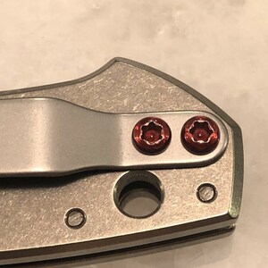 May include: Close-up of a silver pocket knife with two red screws.