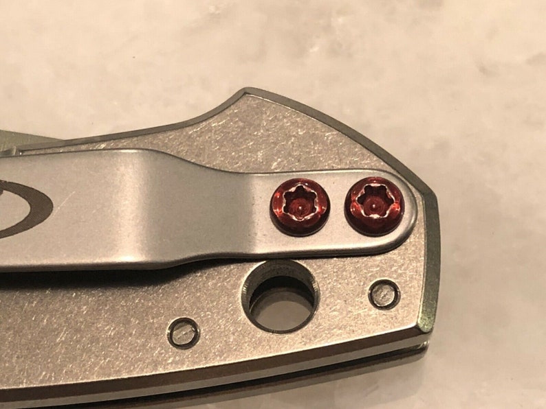 May include: Close-up of a silver pocket knife with two red screws.