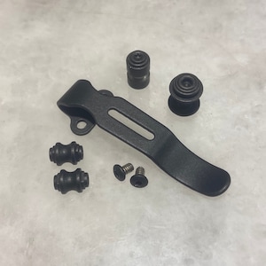 Puede incluir: Clip de bolsillo de metal negro con dos tapones de goma negros, dos tornillos negros y un botón de metal negro.