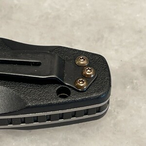 May include: Close-up of a black pocket knife with a silver trim and four gold screws.