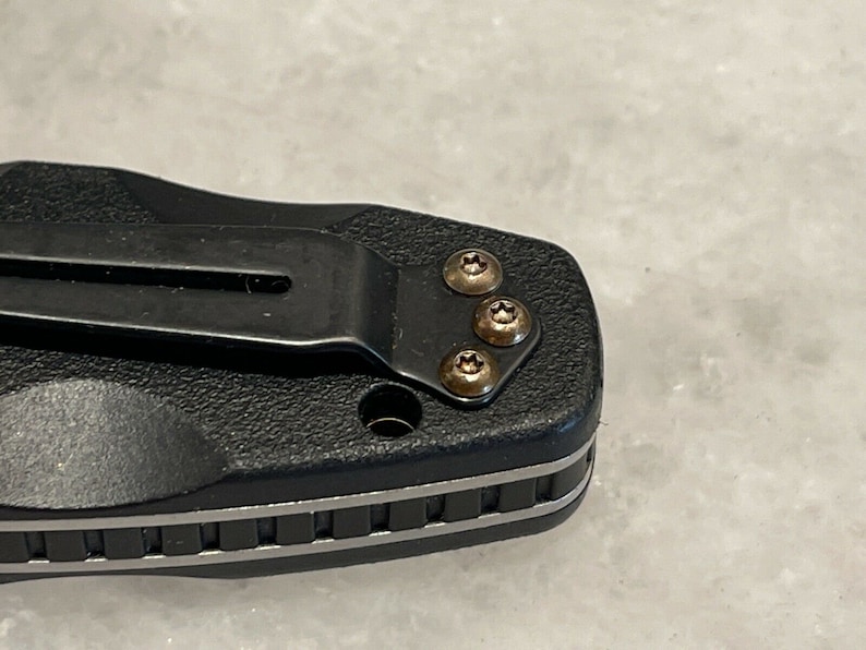 May include: Close-up of a black pocket knife with a silver trim and four gold screws.