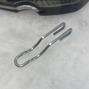 May include: A silver metal shoe lace hook with a curved design.