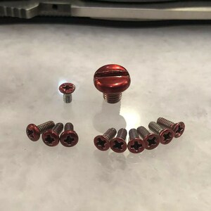 May include: A set of red screws with a cross-shaped head. The screws are arranged in a circle around a larger red screw with a flat head.