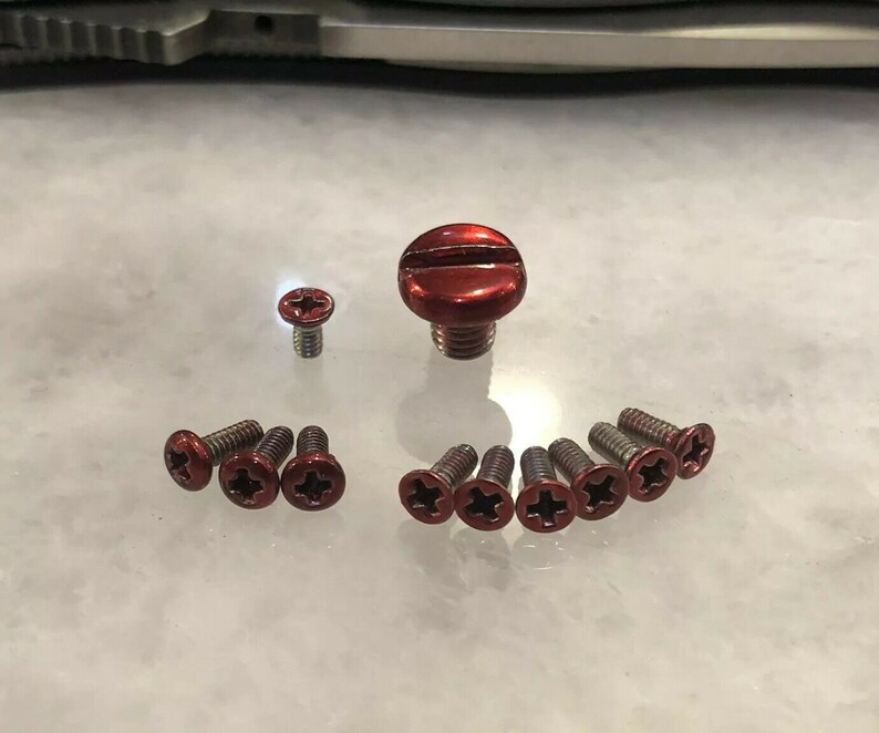 May include: A set of red screws with a cross-shaped head. The screws are arranged in a circle around a larger red screw with a flat head.
