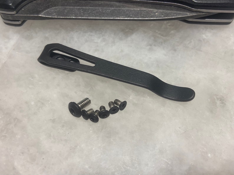 May include: A black metal pocket clip with a curved design and six small black screws.