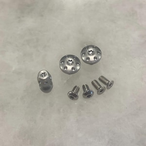 May include: A set of six silver-toned screws and two silver-toned round caps with a star-shaped indentation in the center.