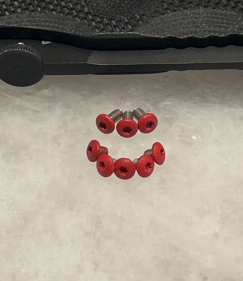 May include: Seven red star-shaped screws with silver bases. The screws are arranged in a semi-circle shape.