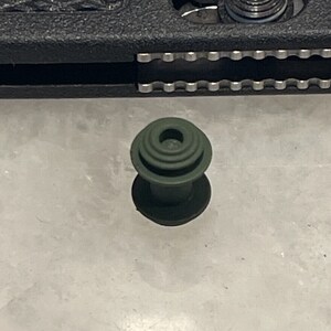 May include: A dark green plastic bottle stopper with a circular top and a ridged base.