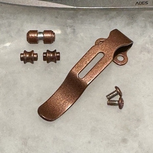 May include: A copper-colored pocket clip with two screws and three small copper-colored hardware pieces.
