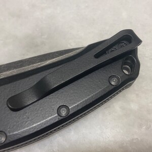 May include: Black pocket knife with a black clip and a textured handle. The knife has a black pocket clip and a textured handle.
