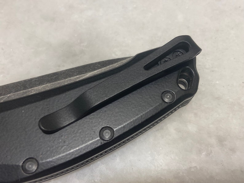 May include: Black pocket knife with a black clip and a textured handle. The knife has a black pocket clip and a textured handle.
