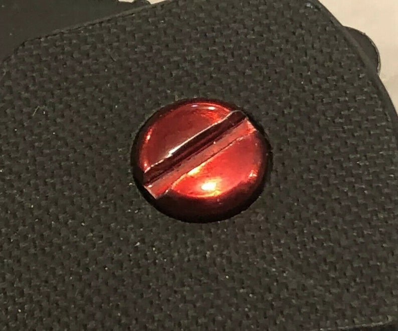 May include: A close-up of a red screw with a single slot on a black textured surface.