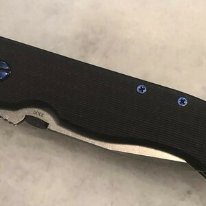 May include: A black folding knife with a black handle and blue screws. The knife has a partially serrated blade and the text "00EE" is visible on the blade.
