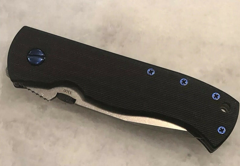 May include: A black folding knife with a black handle and blue screws. The knife has a partially serrated blade and the text "00EE" is visible on the blade.