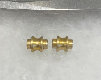 Könnte beinhalten: Zwei kleine, goldfarbene Metallrollen. Die Rollen sind zylindrisch mit einer leichten Rille in der Mitte.