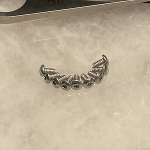 May include: A close-up of ten silver screws with a star-shaped head.