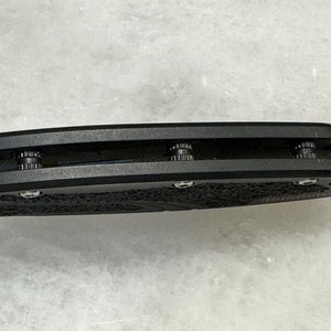 May include: Close-up of a black folding knife with a textured handle and three visible screws.