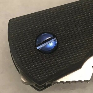 May include: Close-up of a blue screw on a black textured surface. The number 3300 is visible on the surface.