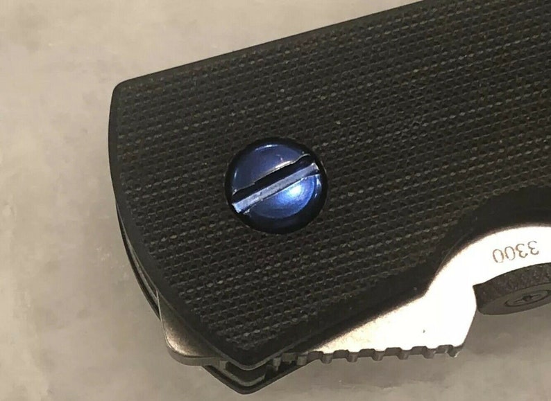 May include: Close-up of a blue screw on a black textured surface. The number 3300 is visible on the surface.