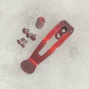 Pu&ograve; includere: Un set di hardware per clip da tasca metalliche rosse, tra cui una clip, viti e un distanziatore a barilotto. La clip ha due fori e un'estremit&agrave; arrotondata. L'hardware &egrave; progettato per un coltello o un oggetto simile.
