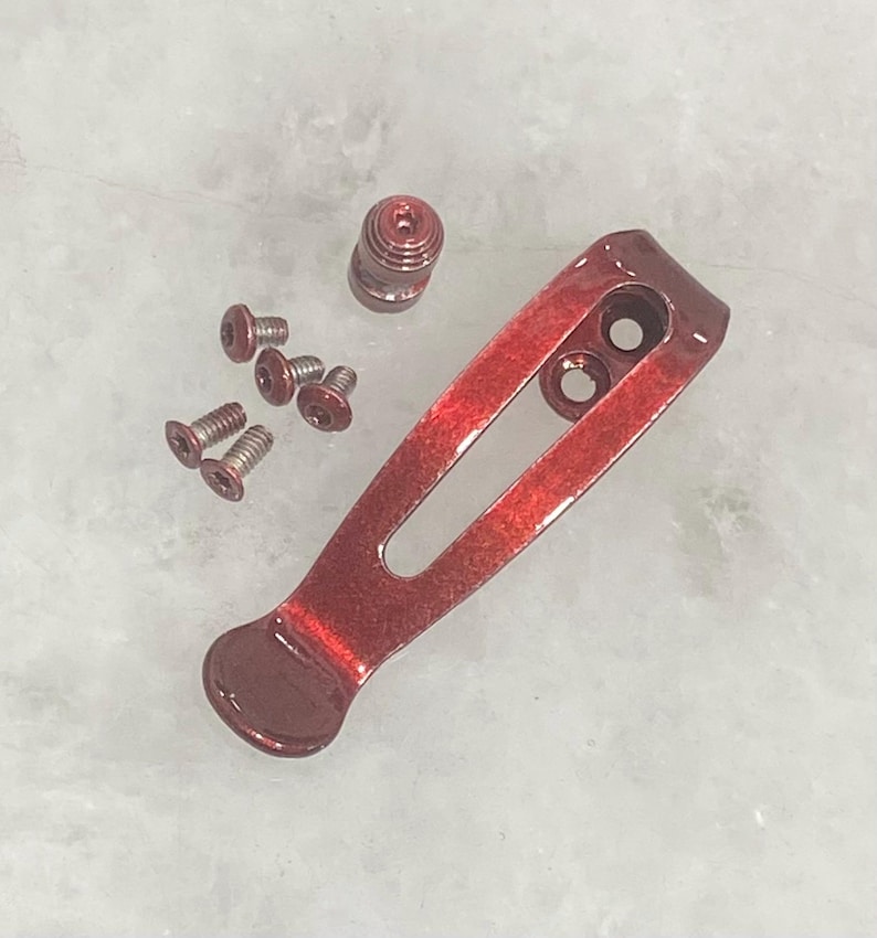 Pu&ograve; includere: Un set di hardware per clip da tasca metalliche rosse, tra cui una clip, viti e un distanziatore a barilotto. La clip ha due fori e un'estremit&agrave; arrotondata. L'hardware &egrave; progettato per un coltello o un oggetto simile.