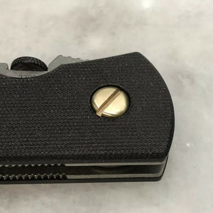 May include: Close-up of a black folding knife with a gold screw. The knife has a textured black handle and a silver blade.