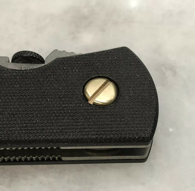 May include: Close-up of a black folding knife with a gold screw. The knife has a textured black handle and a silver blade.