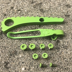 May include: A set of green metal knife scales and pocket clip with a spider design, and six green screws. Two additional screws are also included.