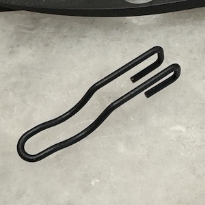 Könnte beinhalten: Schwarzer Metallhaken mit einer gebogenen Form. Der Haken ist zum Aufhängen von Gegenständen an einer Wand oder einer anderen Oberfläche gedacht.