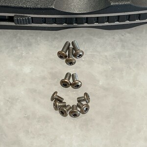 May include: A collection of ten small, bronze-colored screws with a star-shaped head.