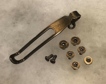 May include: A brass pocket clip with a loop for attaching to a belt or pocket. The clip is accompanied by seven screws, six of which are gold-toned and one is black.