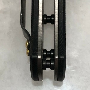 May include: Close-up of a black pocket knife with two silver pivot pins. The knife has a black handle and a silver blade.
