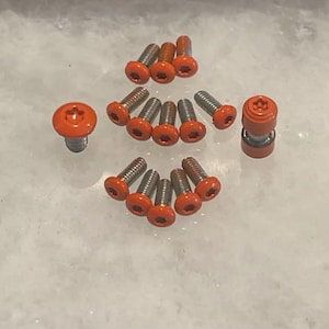 May include: A collection of 13 orange and silver screws with a star-shaped head. The screws are arranged in a circle with one screw in the center.