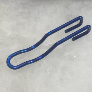 May include: A blue metal hook with a curved shape. The hook is designed to hang items on a wall or other surface.