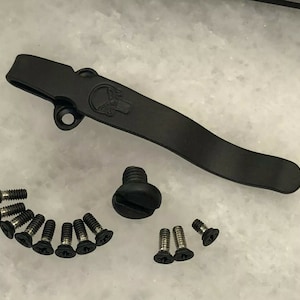 May include: A black metal pocket clip with a skull design, a black screw, and 12 black screws.