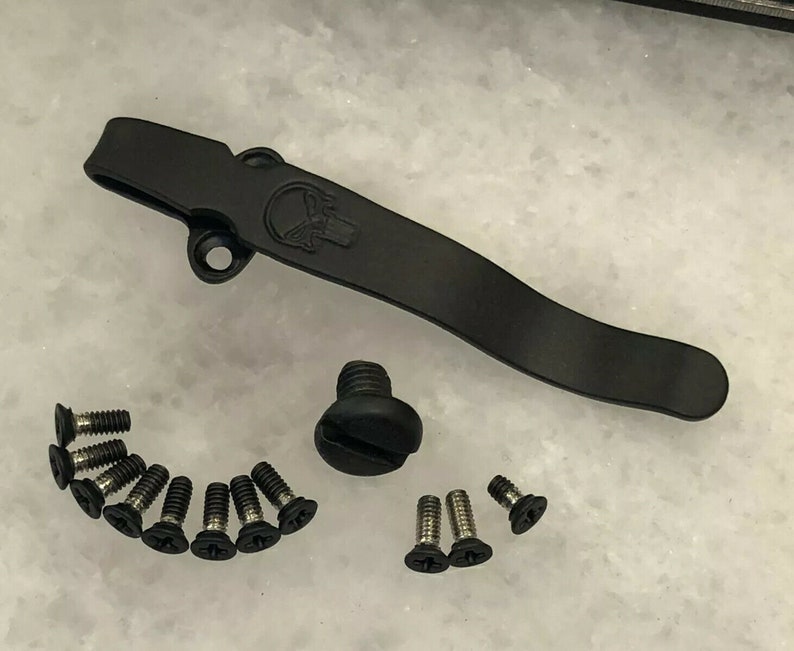 May include: A black metal pocket clip with a skull design, a black screw, and 12 black screws.