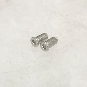 May include: Two silver-colored screws with a star-shaped indentation on the head. The screws have a threaded shaft and are designed for fastening. The image is taken against a white background.