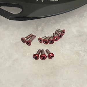 May include: A close-up of ten red star-shaped screws. The screws are arranged in a semi-circle on a white surface.