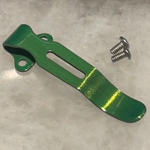 May include: A green metal pocket clip with two silver screws. The clip is designed to attach to a pocket or belt.