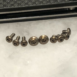 May include: Close-up of a set of ten small, silver-toned screws with a star-shaped head.