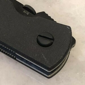 Puede incluir: Primer plano de una navaja de bolsillo negra con un mango texturizado y una hoja plateada. La navaja tiene un peque&ntilde;o tornillo en el mango y el n&uacute;mero "2270" es visible en el lateral.