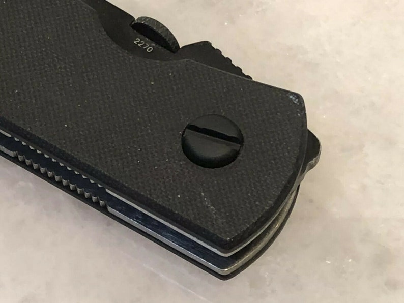 Puede incluir: Primer plano de una navaja de bolsillo negra con un mango texturizado y una hoja plateada. La navaja tiene un peque&ntilde;o tornillo en el mango y el n&uacute;mero "2270" es visible en el lateral.