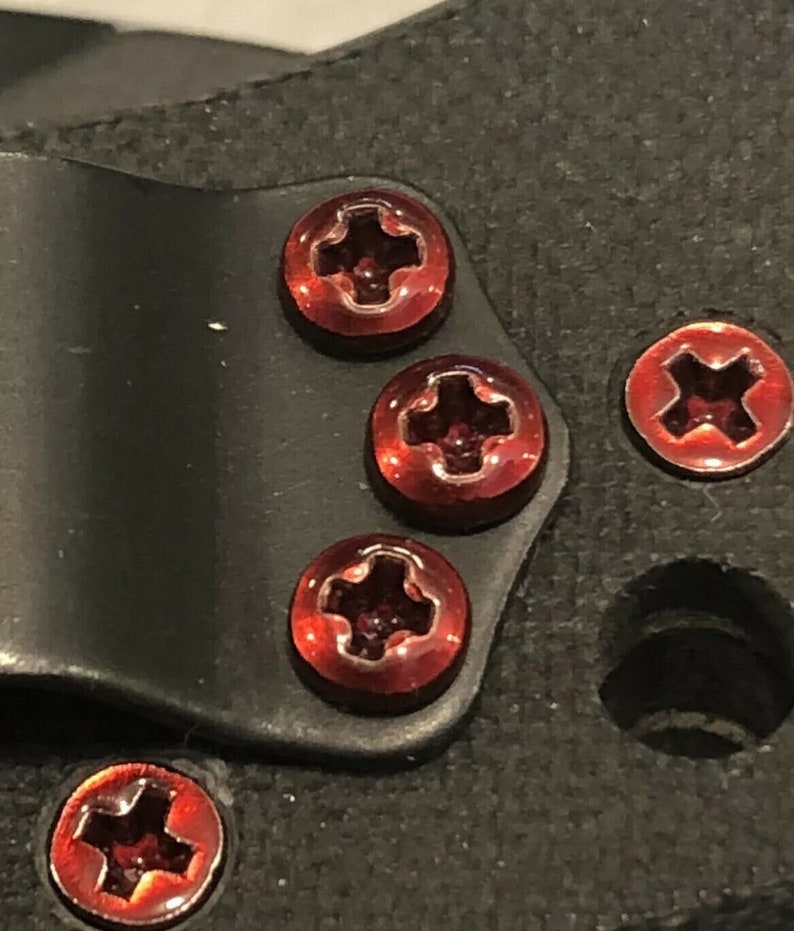 May include: Five red screws with a cross-shaped head are attached to a black surface. The screws are shiny and have a metallic finish.