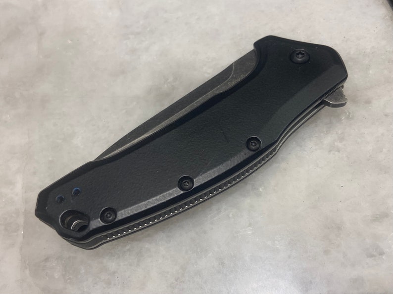 May include: A black folding knife with a textured handle and a partially serrated blade.
