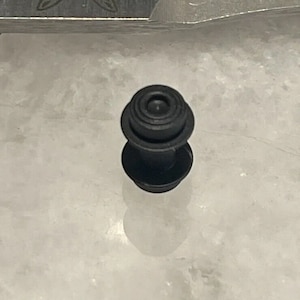May include: A black rubber grommet with a circular top and a cylindrical base.