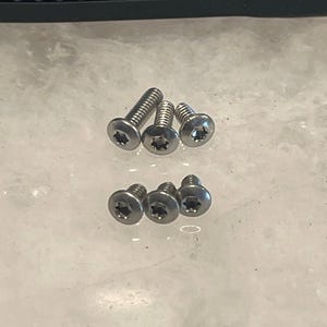 May include: A set of seven silver-toned screws with a star-shaped head. The screws are arranged in two rows on a white surface.