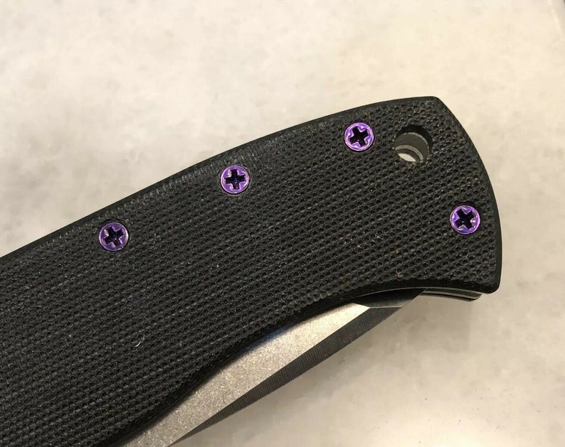May include: Close-up of a black pocket knife with purple screws. The knife has a black handle and a silver blade.
